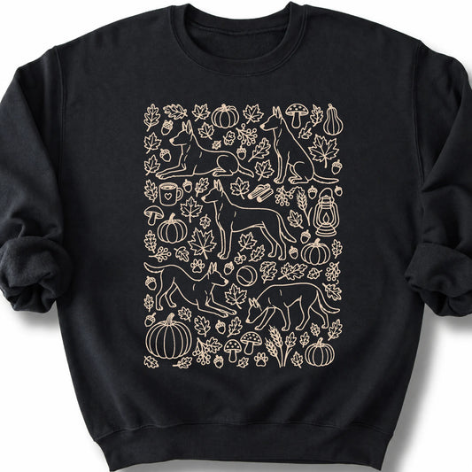 Belgian Malinois among autumn leaves and seasonal icons on a black sweatshirt.