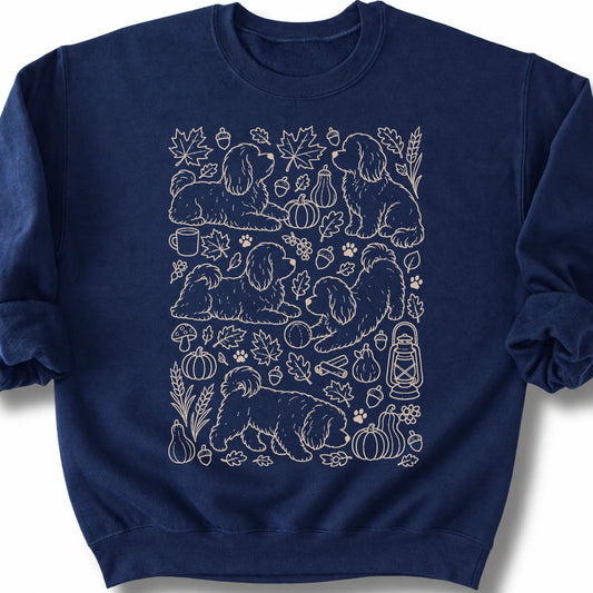 Havanese among autumn leaves and seasonal icons on a navy sweatshirt.