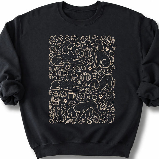 Poodle among autumn leaves and seasonal icons on a black sweatshirt.