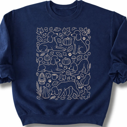 Poodle among autumn leaves and seasonal icons on a navy sweatshirt.