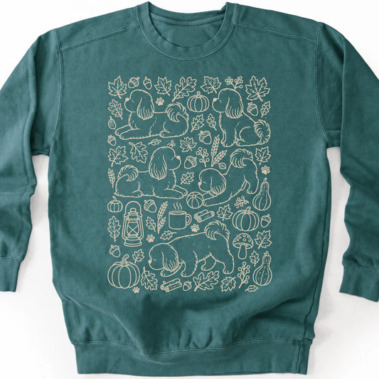 Shih Tzu among autumn leaves and seasonal icons on a blue spruce sweatshirt.