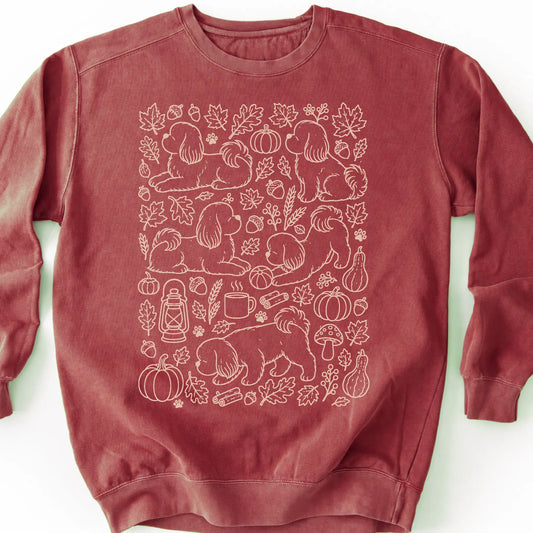 Shih Tzu among autumn leaves and seasonal icons on a crimson sweatshirt.