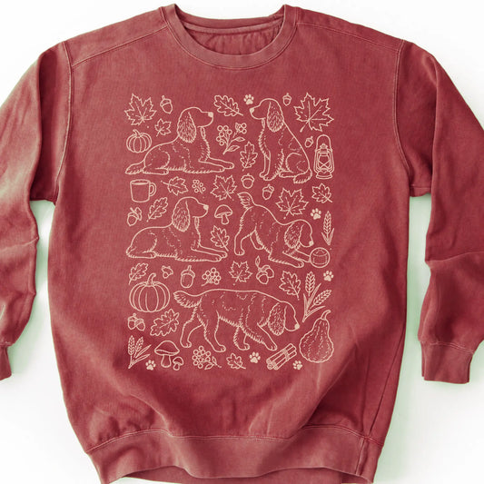 Springer Spaniel among autumn leaves and seasonal icons on a crimson sweatshirt.