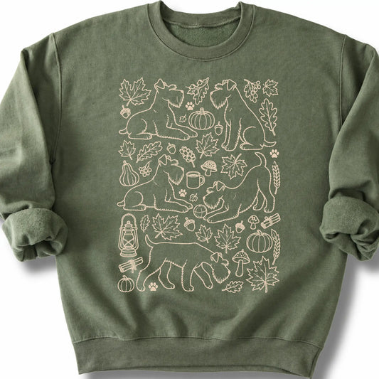 Standard Schnauzer among autumn leaves and seasonal icons on a military green sweatshirt.