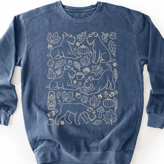 Standard Schnauzer among autumn leaves and seasonal icons on a denim sweatshirt.
