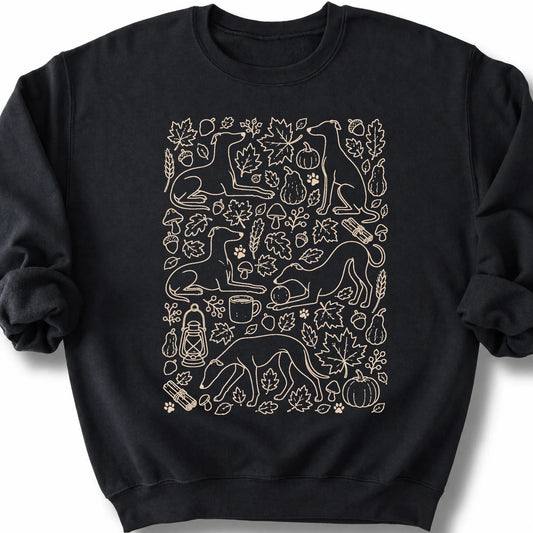 Whippet among autumn leaves and seasonal icons on a black sweatshirt.