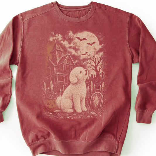 Bichon Frise beside a haunted house on a crimson sweatshirt.