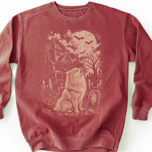 Pomeranian beside a haunted house on a crimson sweatshirt.